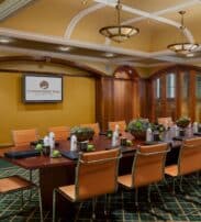 A conference room with a long table, tan chairs, notepads, bottled water, small plants, and a wall-mounted screen displaying "O'Donoghue Ring Collection.