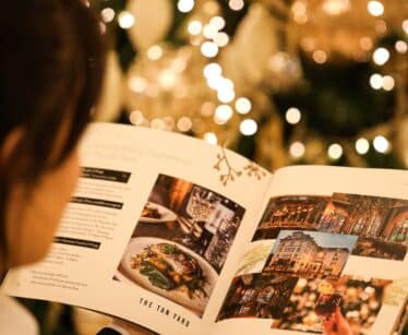 Person reading a magazine featuring food and restaurant images in front of a decorated, lit Christmas tree.