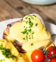 A plate with eggs Benedict topped with hollandaise sauce and chopped chives, served with vine cherry tomatoes.