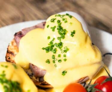A plate with eggs Benedict topped with hollandaise sauce and chopped chives, served with vine cherry tomatoes.