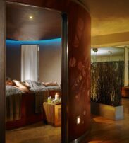 A person lies face down on a massage table in a dimly lit spa room with candles, towels, and calming décor.