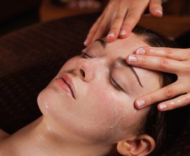 Person receiving a facial massage whilst lying down, with hands gently massaging their forehead and cream applied to their face.