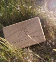 A rectangular wooden box with "Inish Living" and a minimalist logo etched on the lid sits in tall, sunlit grass.