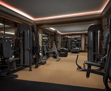 A modern gym with various exercise machines, including strength training equipment and exercise bikes, set on a beige carpet with mirrors on the walls.
