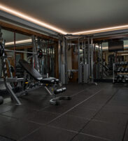 Modern gym room with weight benches, dumb-bells, barbells, cable machine, mirrored walls, and rubber flooring.