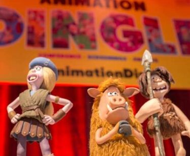 Three clay animation figures are on display in front of a colourful "ANIMATION DINGLE" sign at an animation event.