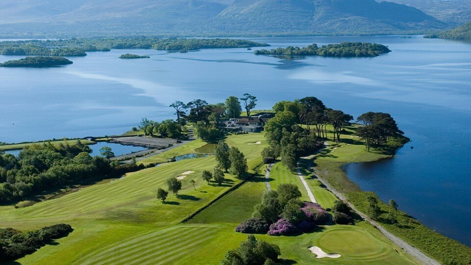 Scenic golf course and mountains by a tranquil lake, luxury hotel in lush greenery, ideal for relaxation and golfing getaways.
