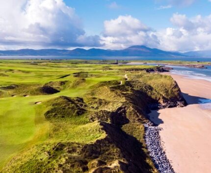Stunning coastal golf course with mountainous backdrop and sandy beach.