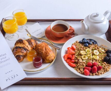 Luxurious breakfast tray with fresh pastries, fruit granola, juices, and tea in an elegant hotel room setting.