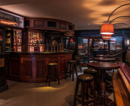 Cosy hotel bar with wooden stools, warm lighting, stocked shelves; perfect for relaxing and socialising.