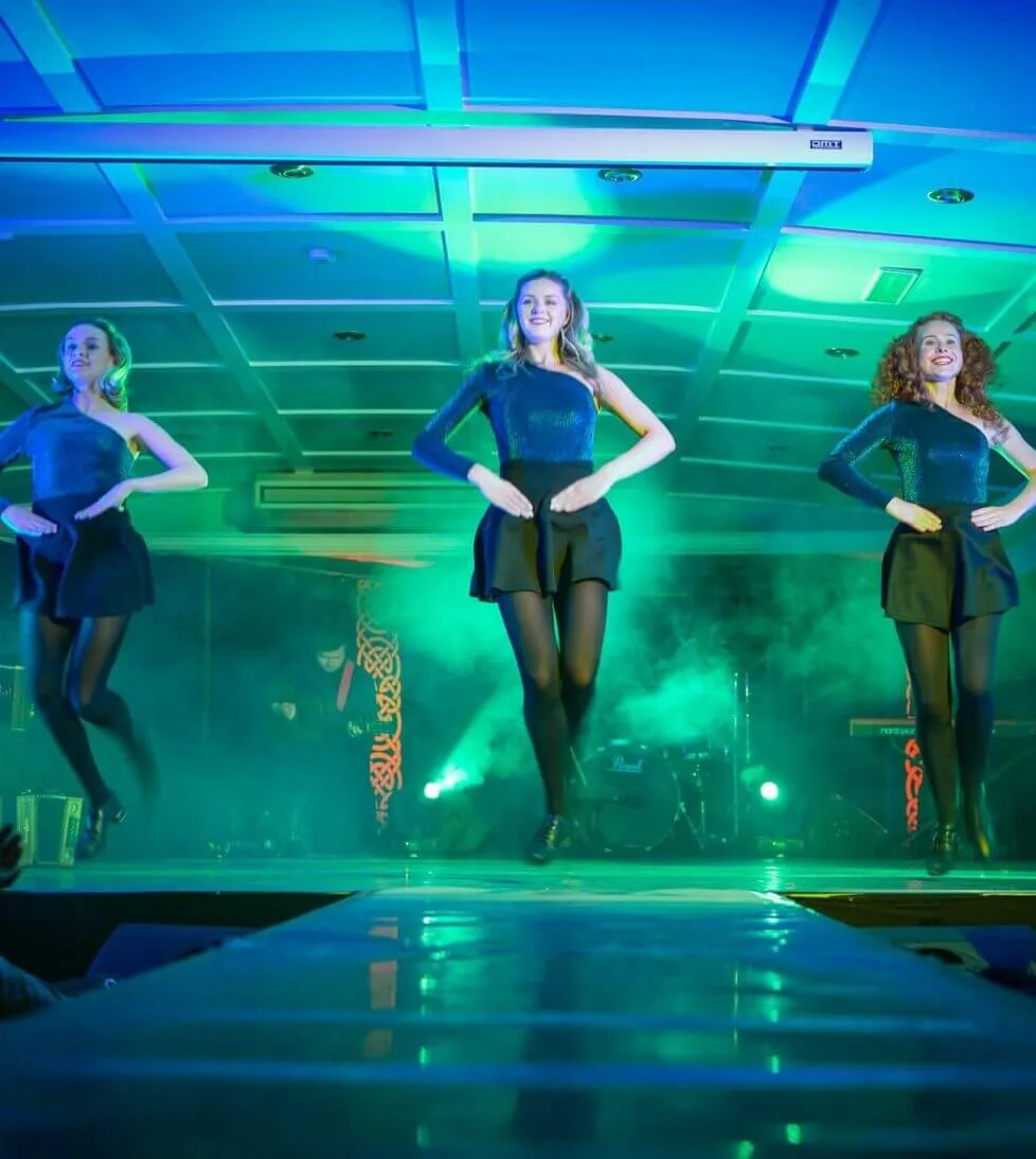 Energetic dancers performing live Irish show in hotel banquet hall with vibrant lighting and elegant decor.