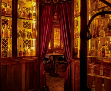 Cosy hotel bar with warm lighting, wooden shelves of premium spirits, velvet curtains, inviting guests for a relaxing evening.