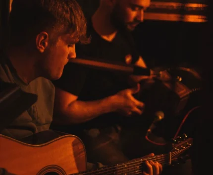 Warm, cosy pub setting with live acoustic music; two musicians playing guitar and accordion. Perfect for a relaxing evening.