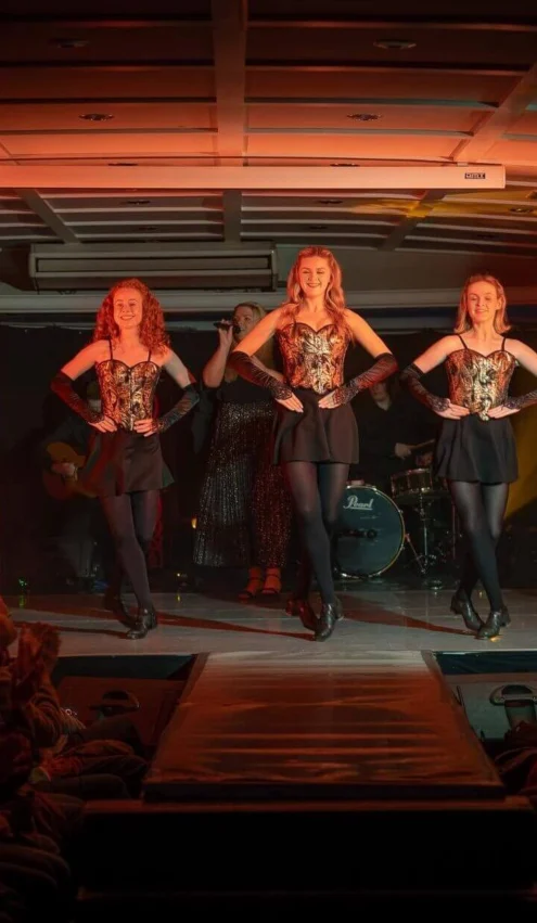 Guests enjoying lively Irish step dancing performance in hotel theatre with vibrant lighting and enthusiastic audience.