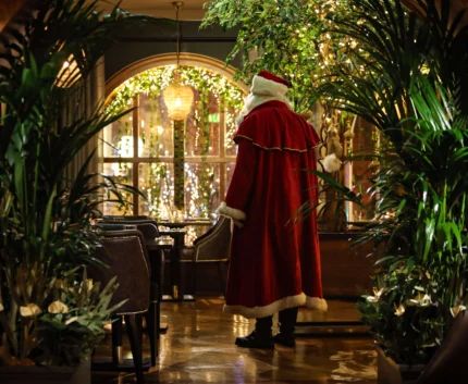 Festive hotel lounge with Christmas lights, greenery and a Santa-costumed figure by dining tables and plush chairs