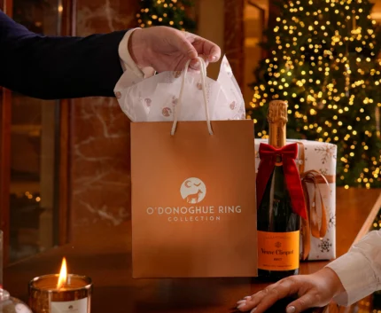 Festive hotel reception with O'Donoghue Ring gift bag, champagne bottle with red bow, lit candle and Christmas trees